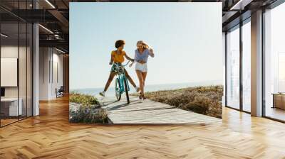 Two women having fun with a bicycle at beach Wall mural