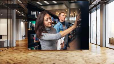 university students taking book from shelf in library Wall mural