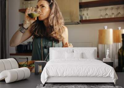 Vegan woman drinking green juice in her kitchen Wall mural