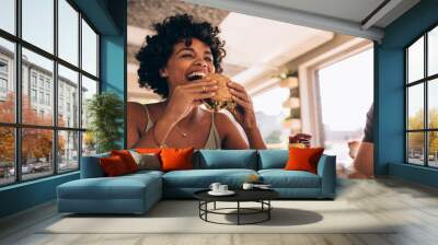 Woman enjoying eating burger at restaurant Wall mural