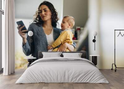 Woman holding her baby and texting on her phone Wall mural