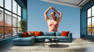 Woman in sportswear stretching her arms outdoors Wall mural