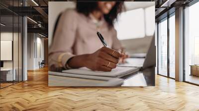 Woman making notes looking at laptop working from home Wall mural