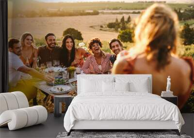 Woman taking picture of friends having dinner party Wall mural