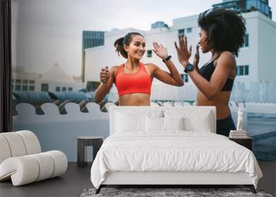 Women athletes giving high five while running on rooftop Wall mural