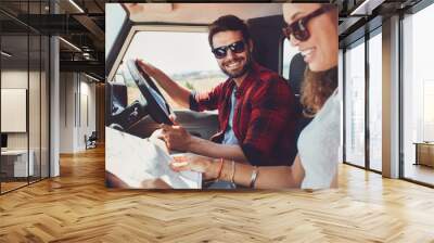 Young couple sitting inside their car with map Wall mural