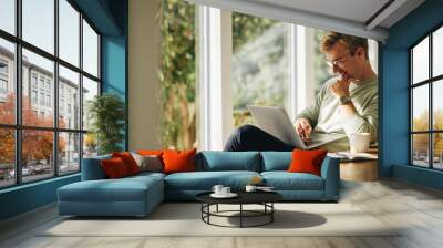 Young man using laptop and smiling Wall mural