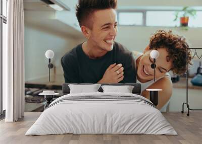 Young queer couple laughing cheerfully in their kitchen Wall mural