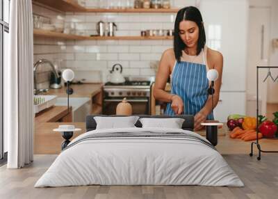 Young woman cutting vegetables in kitchen at home Wall mural