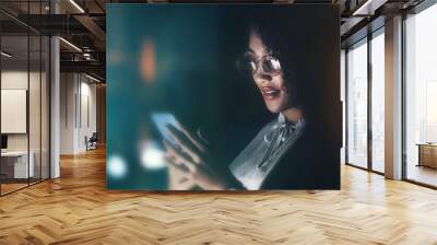 Businesswoman, phone and communication at night for networking, chatting or texting on dark background. Female employee holding smartphone working late at the office for online planning strategy Wall mural