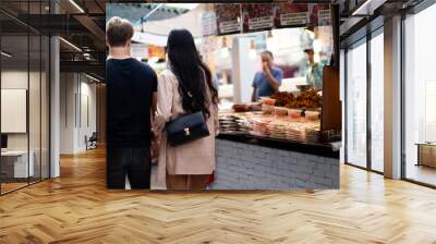 Asian woman and Caucasian Man from diverse culture shopping and eating street food outdoor during vacation and travel in Summer together, blur background selective focus Wall mural