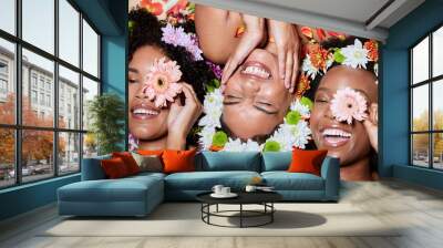 Top view, beauty and black women with flowers for skincare in studio on brown background. Makeup aesthetics, organic cosmetics and group, friends or female models with floral plants for healthy skin Wall mural