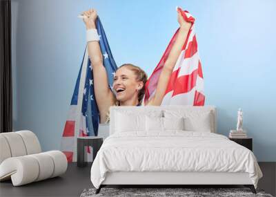 Young fit female athlete cheering and holding American flag after competing in sports. Smiling fit active sporty woman feeling motivated and celebrating achieving gold medal in olympic sport Wall mural