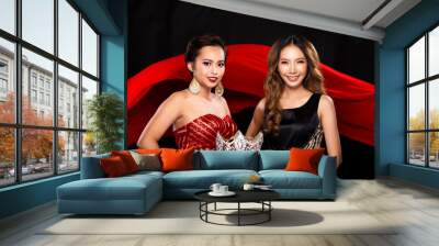 Two Finalist of Miss Beauty Pageant Queen Contestants happy smile for a jewel Diamond Crown. They wear Sequin Long Gown and watch prize on pillow in background of red cloth flying in Air Wall mural