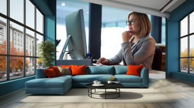 Computer, thinking and business woman in office working late on project at night alone. Desktop, professional and female person problem solving, focus or solution, planning or reading on deadline Wall mural