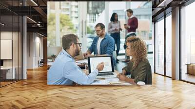 Enhancing a collaborative effort with online resources. Shot of two young colleagues using a laptop together in a modern office. Wall mural