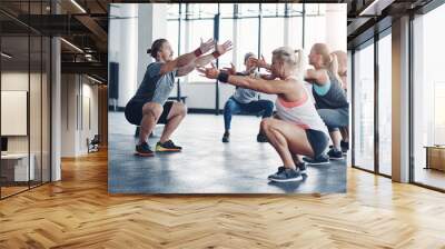 Hes the one to get you in shape. Shot of a fitness instructor working with a group of people at the gym. Wall mural