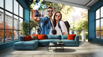 Selfie, happy couple and outdoor for travel with a smile for holiday memory and happiness. Man and woman at a park with trees for adventure, journey or vacation photo and freedom with love and care Wall mural