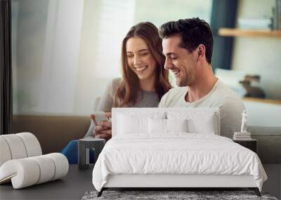 Sharing is caring. Shot of a happy young couple using a phone together on the sofa at home. Wall mural