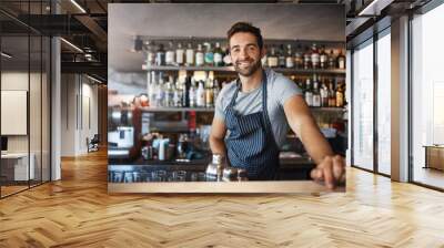 Drinks on me. Portrait of a confident young man working behind a bar counter. Wall mural