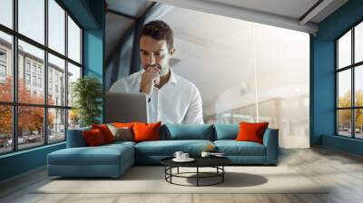 Im gonna have to think about this.... Cropped shot of a handsome young businessman looking thoughtful while working on his laptop in the office. Wall mural