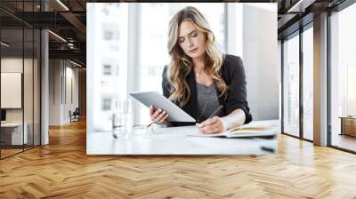 Multitasking makes it happen. Shot of a young businesswoman using a digital tablet and writing notes at her desk in a modern office. Wall mural