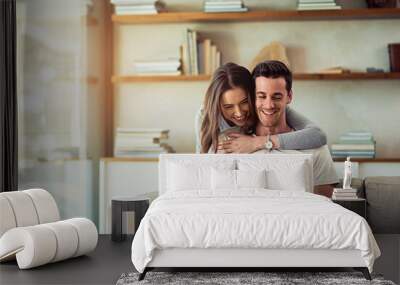 Show love everyday, in the simplest of ways. Shot of a young woman hugging her husband while he uses a laptop on the sofa at home. Wall mural