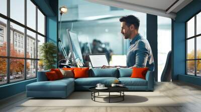 Success happens when you combine will with skill. Shot of a young businessman using a computer at his desk in a modern office. Wall mural