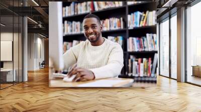 The internet has some great research information too. Portrait of a young man using a computer in a college library. Wall mural