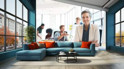 True creativity doesnt age. Portrait of a happy designer sitting at her desk while her colleagues work in the background. Wall mural