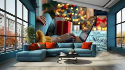 Cozy scene, woman typing on laptop at home during Christmas. Girl is ordering Christmas gifts online for her loved ones. Concept of holiday ambiance, festive decorations, e-commerce, online shopping Wall mural