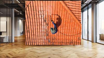 A person outdoors cleaning the red clay roof using a high pressure washer. Professional washing house tiles with water hose. Wall mural