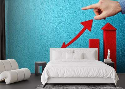 A hand points at a rising red bar graph against a blue background, symbolizing growth and progress. Wall mural