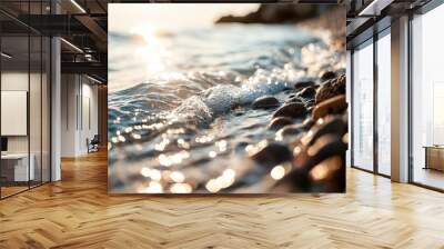 Gentle waves lap against smooth pebbles, reflecting sunlight in a serene coastal scene at dusk. Wall mural