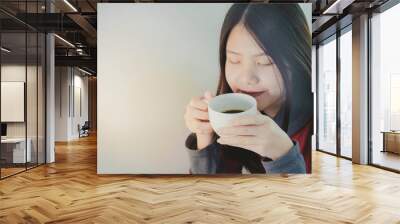 Beautiful asian woman enjoys drinking a cup of hot coffee during winter time. White plain background, space for text. Wall mural