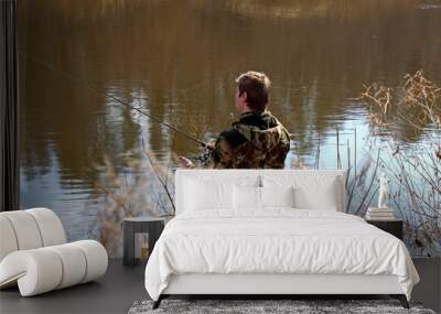 Fisherman in camouflage clothing, fishing on spinning. Wall mural