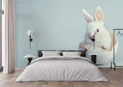 A cute rabbit peeking its head from a cracked Easter egg with a white blue background Wall mural