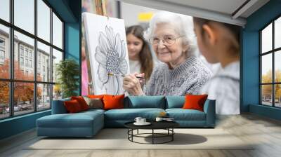 An elderly woman is painting in an art class, with a young female teacher and other students also working on their paintings in the background Wall mural