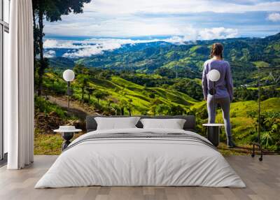 girl stands on hill admiring idyllic landscape of Costa Rican mountains; green slopes bathed in clouds in Costa Rica Wall mural