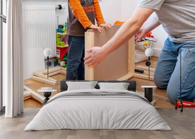 Father and son assembling flat pack furniture. A set of two small chairs with desk in boys bedroom. Wall mural