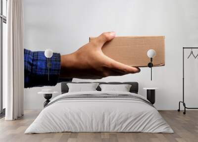 A hand holding a cardboard box against a gray background, illustrating the concept of shipping, delivery, and logistics services Wall mural