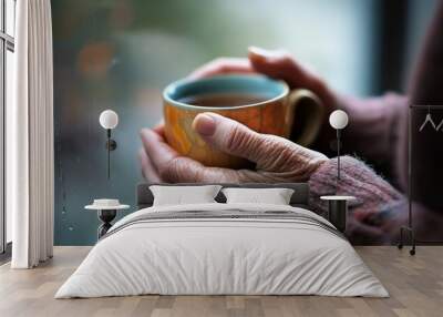 Elderly hands hold warm tea by a window. Wall mural