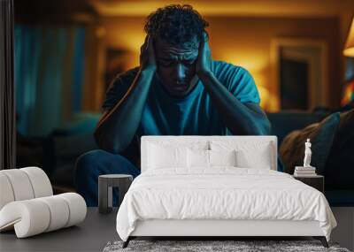 A man sitting on the couch with his head in hands, looking distressed and emotional, showing signs of anxiety or depression. The concept of emotional pain and suffering due to life events. Wall mural