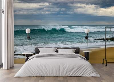 Turquoise wave crashing on beach set against an angry stormy sky Wall mural