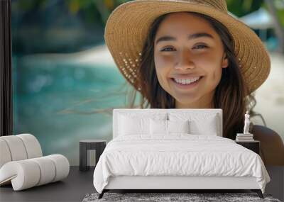 Portrait of a beautiful young woman in a straw hat smiling at the camera on a tropical beach, with a blue sky and white sand background. Summer vacation concept. Wall mural