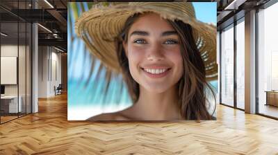 Portrait of a beautiful young woman in a straw hat smiling at the camera on a tropical beach, with a blue sky and white sand background. Summer vacation concept. Wall mural