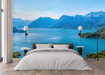 Stunning panoramic view of clear blue lake surrounded by lush green mountains under a bright blue sky. Wall mural