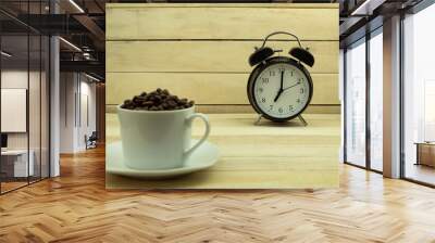 Alarm clock and roasted coffee beans in a white cup as a background Wall mural