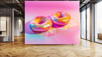 Two colourful neon bagels with a glossy finish on a pastel pink background, creating a vibrant and modern visual. Ideal for artistic food photography, creative culinary projects, and playful designs. Wall mural