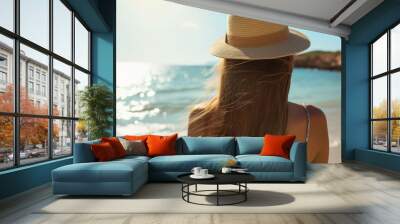 Woman from behind in a straw hat gazing at the sea on a sunny beach. Wall mural